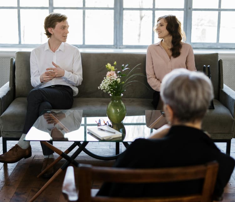 Two people sitting on a couch in front of an older woman.